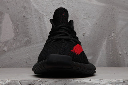 Front view of the black lace-up sneaker with a black toe, red side detail, and textured sole.