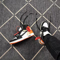 Angled view of the sneaker pair showing black laces, white toe panels, and orange accents.