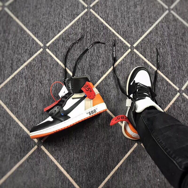 Angled view of the sneaker pair showing black laces, white toe panels, and orange accents.