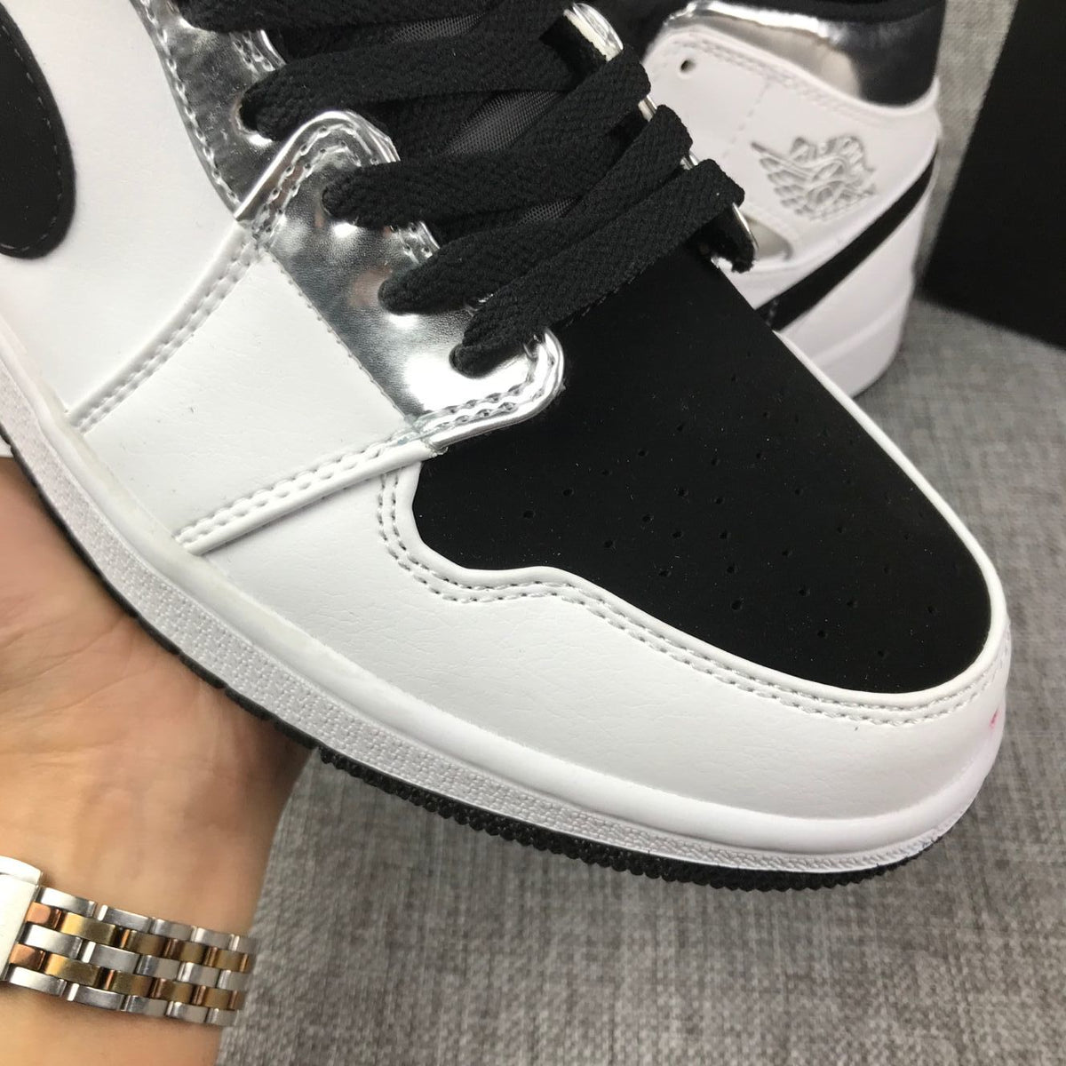 Close-up of the black perforated toe box, black laces, and metallic silver eyelet panel.