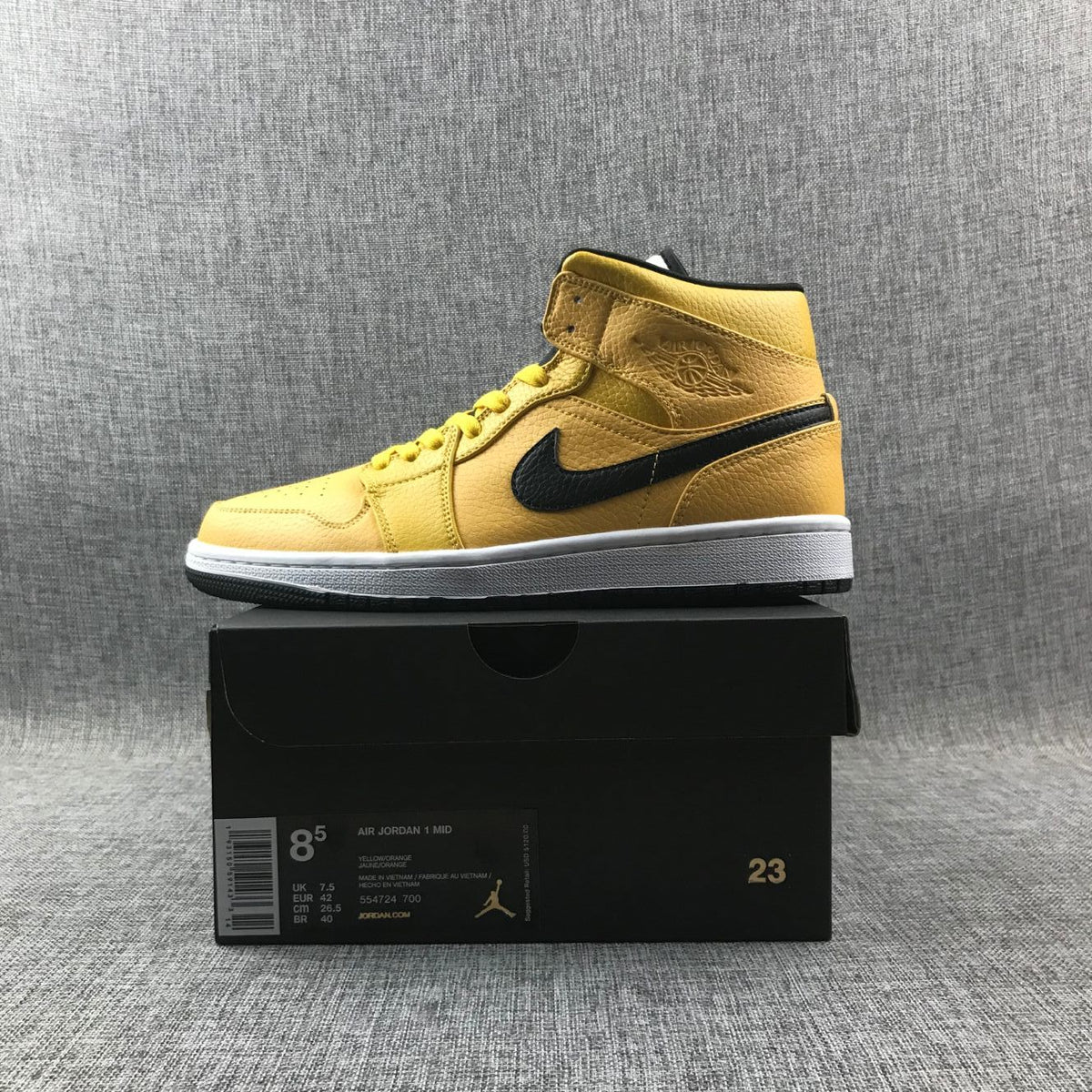 Yellow and black sneaker displayed on a black shoebox; the box label shows Air Jordan 1 Mid, style code 554724-700, and EU 42.