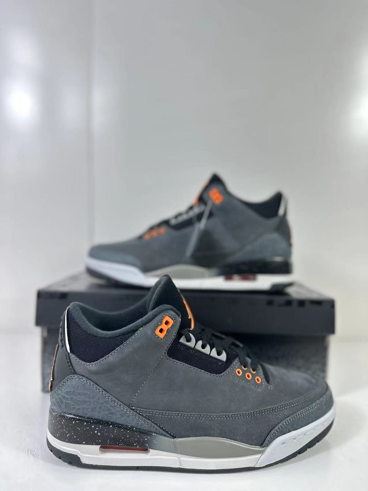 Close three-quarter view of dark gray Air Jordan 3 Retro sneakers with orange accents, elephant-print panels, and a white and black sole.