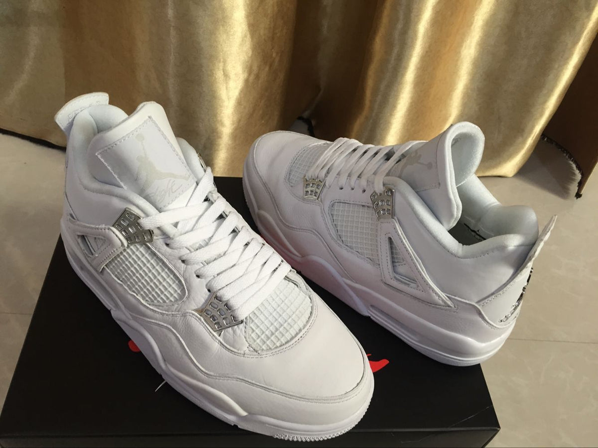 Angled view of the white Jordan 4 pair showing the lace-up construction, padded collars, and textured side panels.