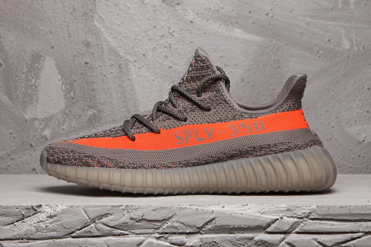 Side profile of a grey Yeezy 350 V2 sneaker with an orange stripe and contrasting translucent ribbed sole.