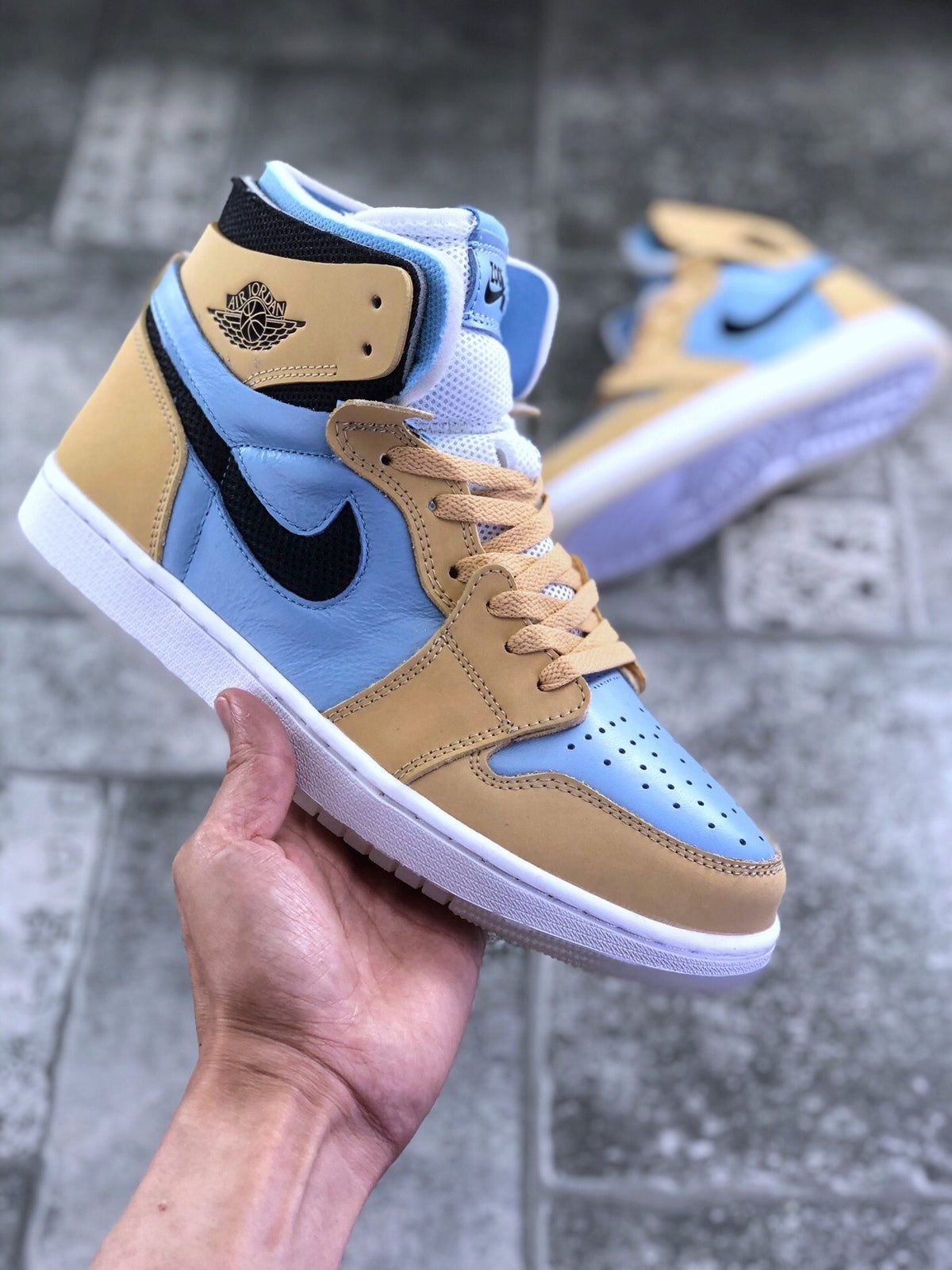 Front three-quarter view of the tan and light blue Jordan high-top sneaker with perforated toe box and tan laces.