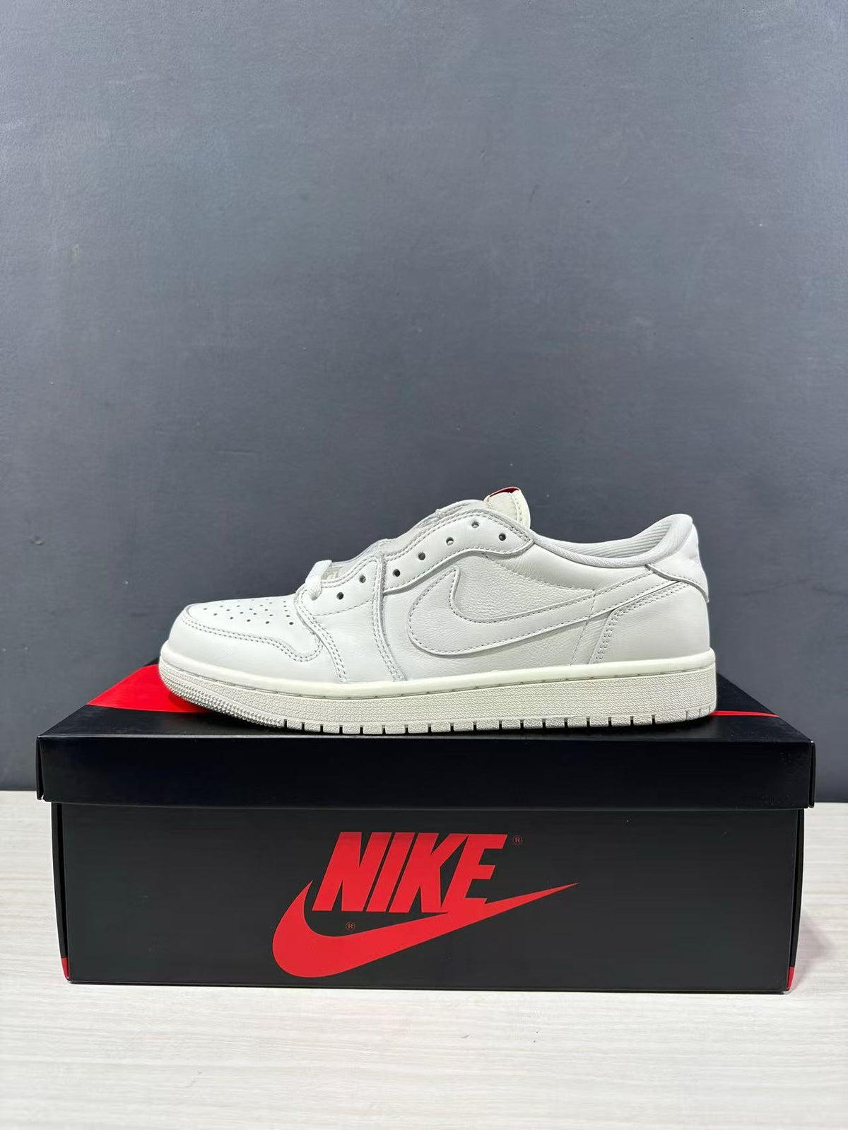 Side profile of a white low-top Jordan sneaker on a shoe box, showing the perforated toe, layered panels, and padded collar.