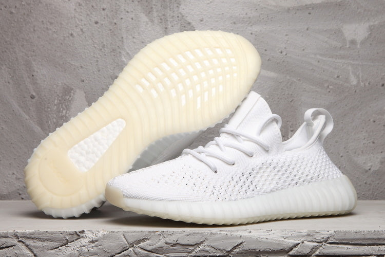 White Yeezy 350 V2-style sneakers shown from the side and outsole, featuring a textured upper and translucent ribbed sole.