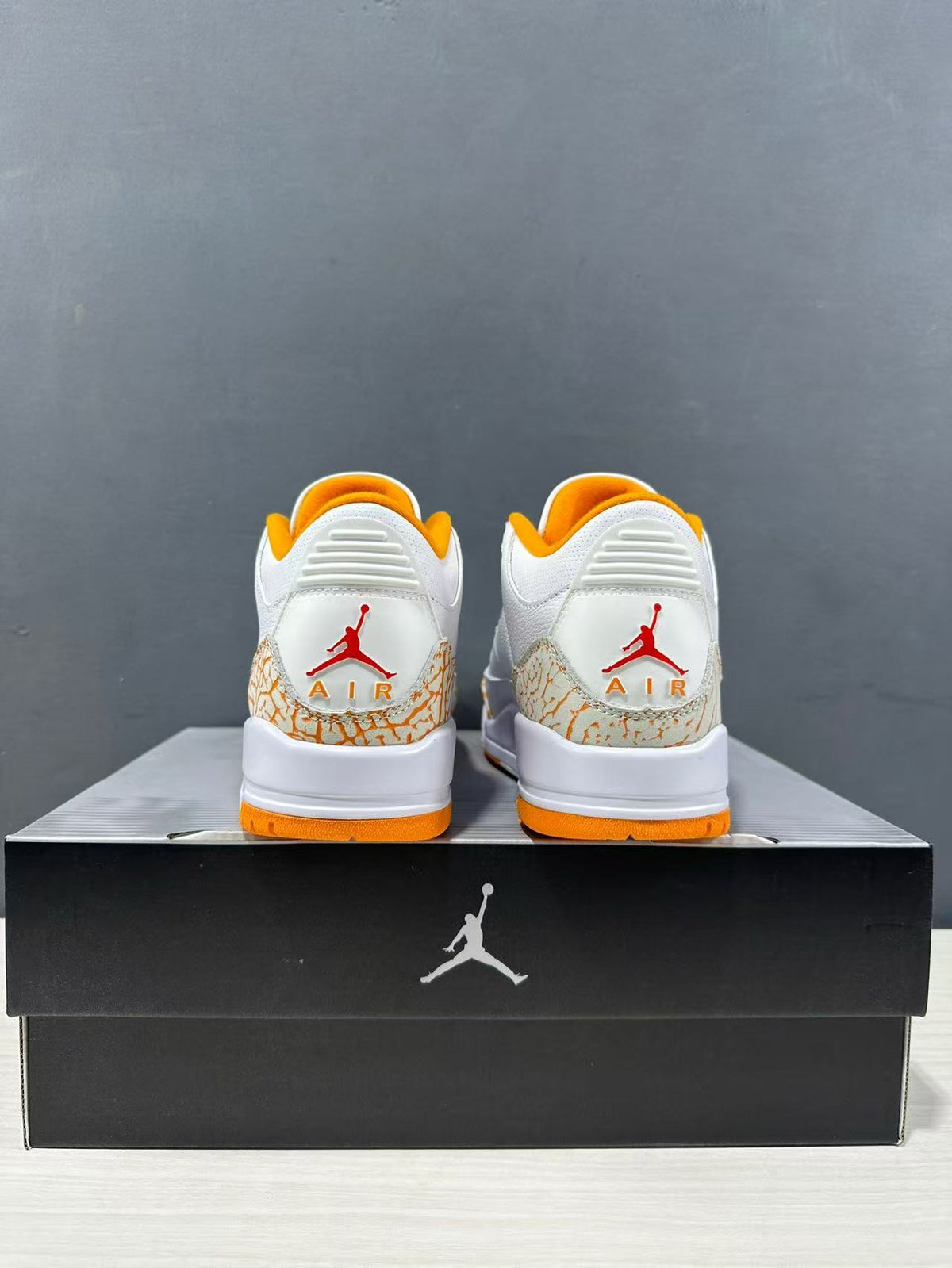Rear view of the pair showing red Jordan branding, orange heel lining and outsole accents, and elephant-print heel panels.