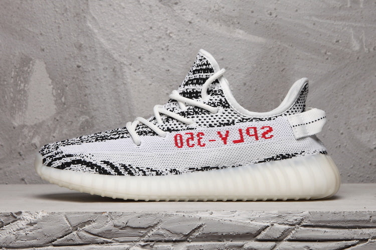 Side profile of a black-and-white knit sneaker with red side lettering and a ribbed light-colored sole.