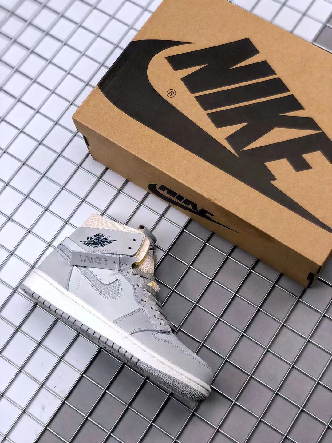 Gray high-top Jordan sneaker beside a Jordan shoebox, showing the side profile and white midsole.