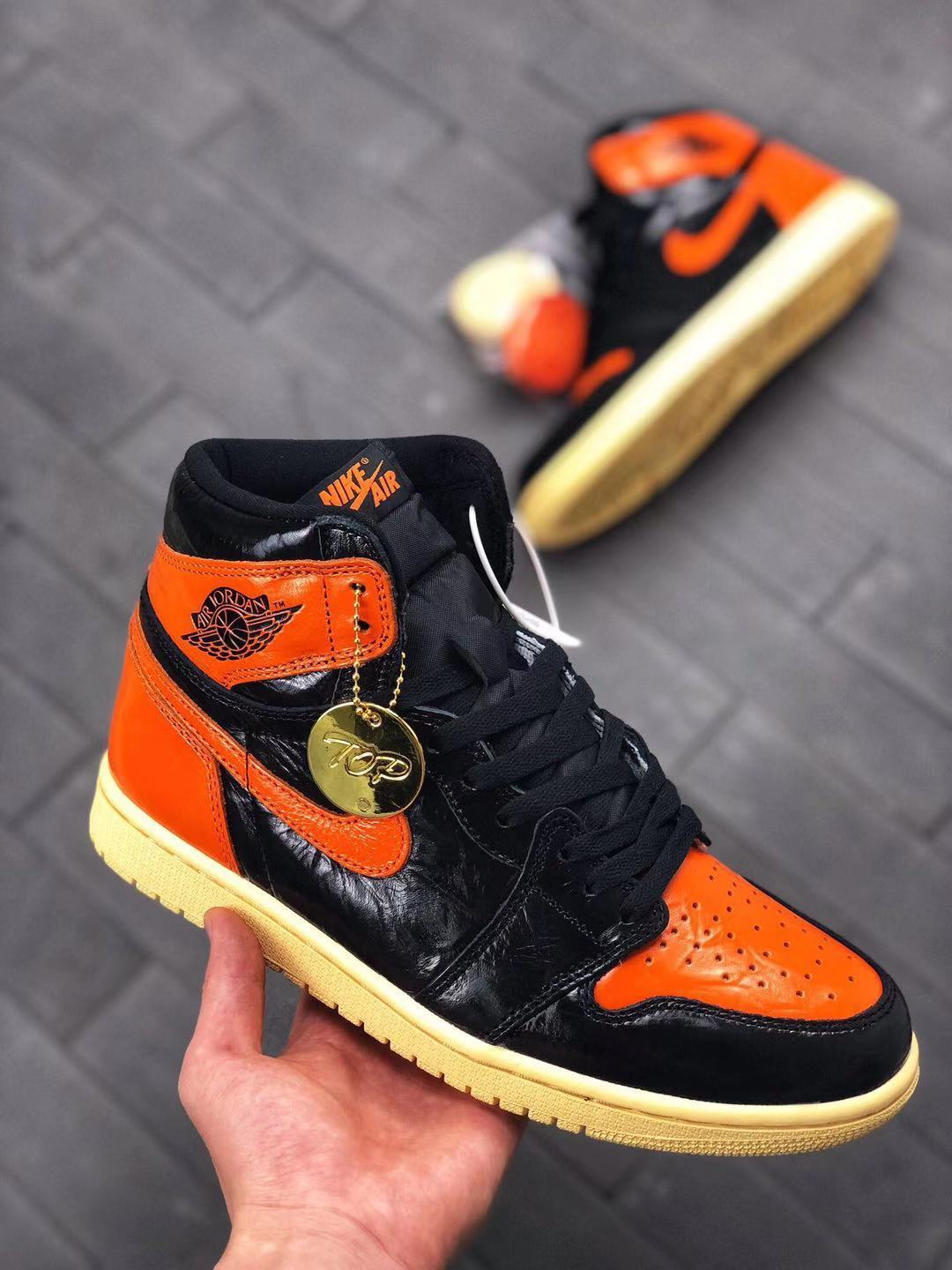 Close-up angled view of the black and orange high-top sneaker with black laces, orange toe panel, and attached hangtag.