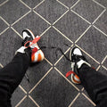 The sneakers being worn, showing the high-top fit, orange outsole accents, and contrasting lace details.