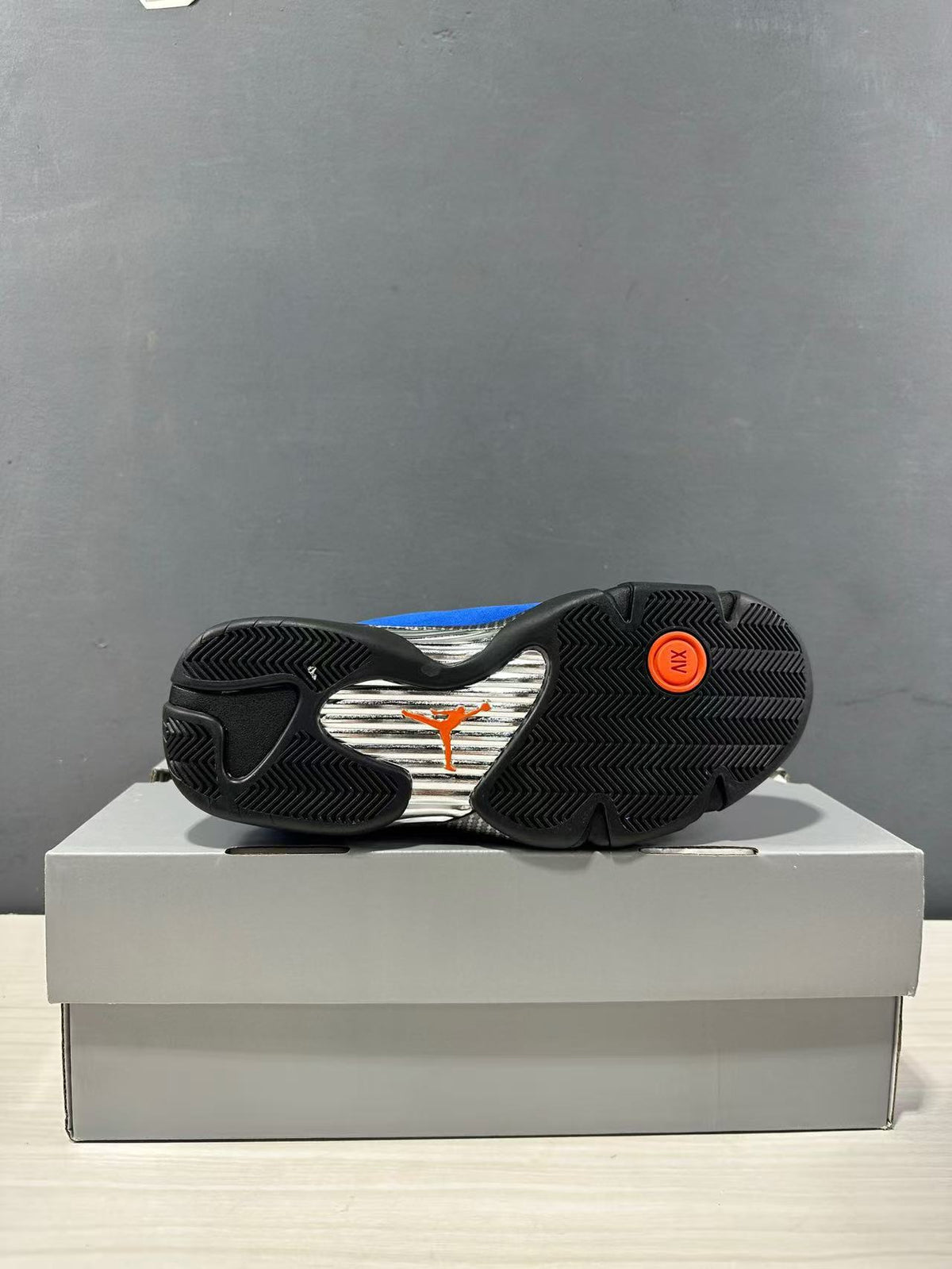 Outsole view of the sneaker showing black patterned rubber sections, a silver center panel, and orange Jordan branding.