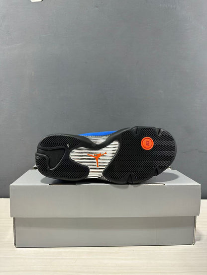 Outsole view of the sneaker showing black patterned rubber sections, a silver center panel, and orange Jordan branding.
