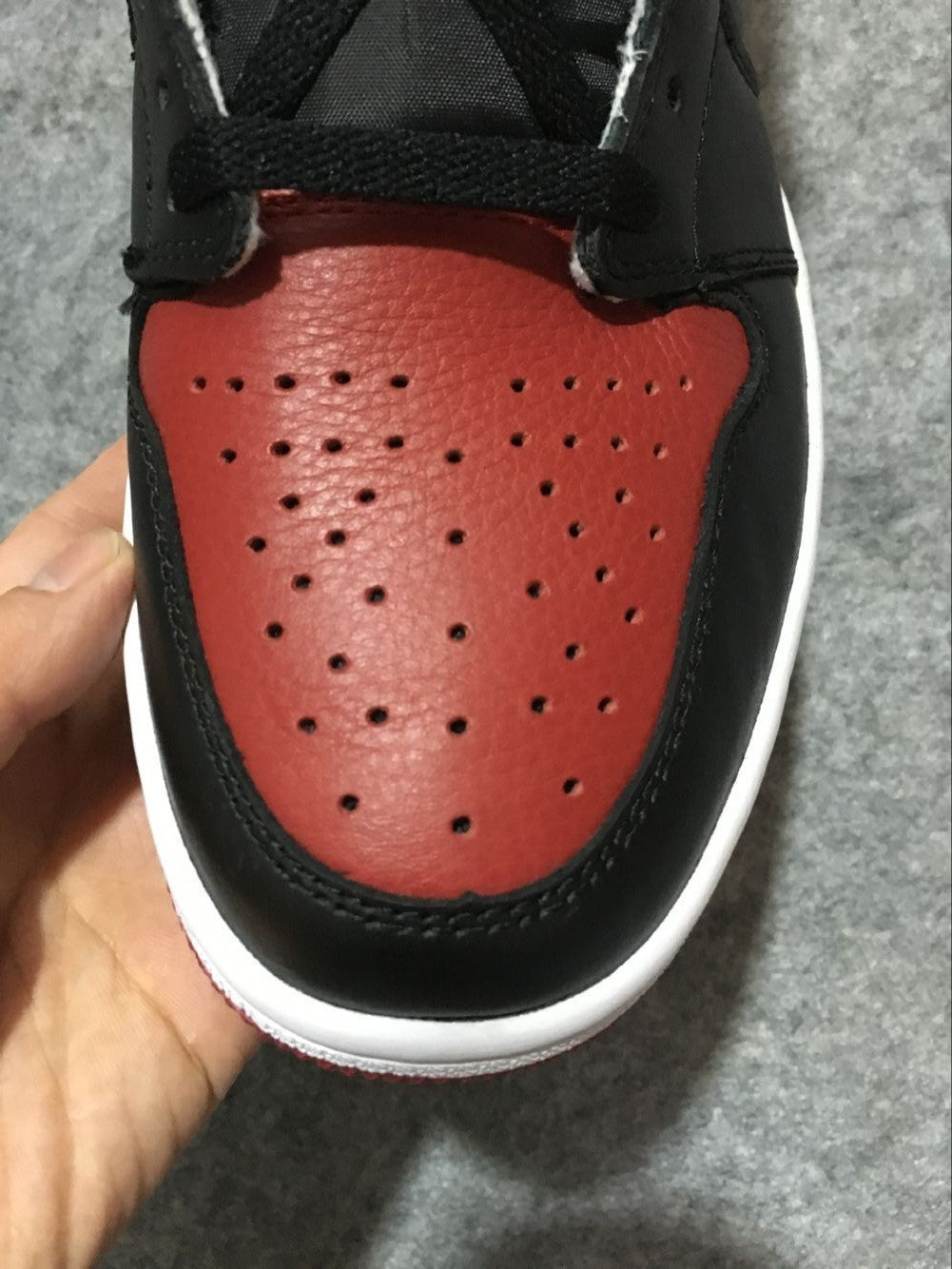 Close-up of the red perforated toe box framed by black overlays and a white sole edge.