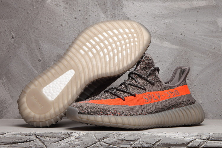 Yeezy 350 V2 sneakers shown from the side and outsole, with a dark grey upper, orange stripe, and translucent ribbed sole.