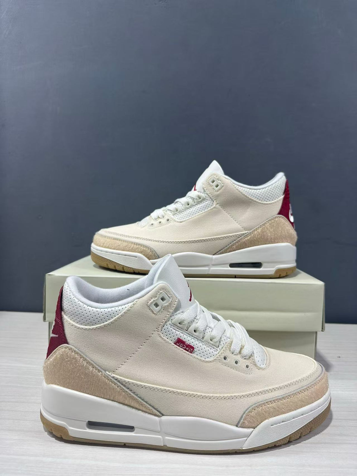 Close angled view of the cream and red Air Jordan 3 Retro sneaker pair highlighting the perforated collar and layered overlays.