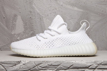 Side profile of a white sneaker showing the textured upper, heel pull tab, and ribbed sole unit.