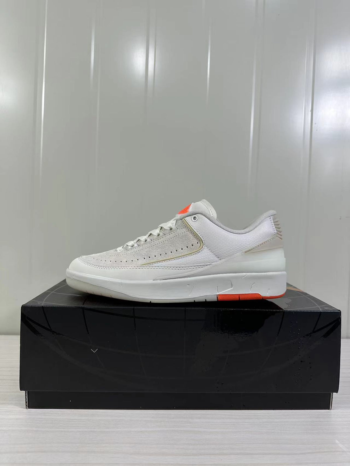 Side profile of the low-top sneaker showing the light beige upper, white midsole, and orange outsole accent.