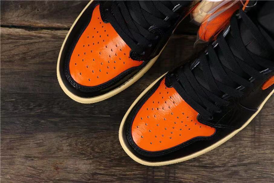 Top view of two sneakers showing orange perforated toe panels, black laces, and contrasting overlays.