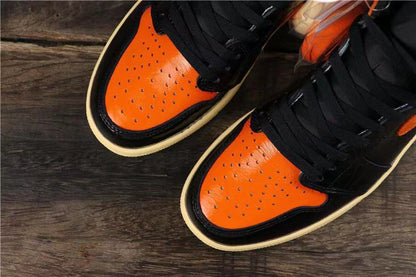 Top view of two sneakers showing orange perforated toe panels, black laces, and contrasting overlays.