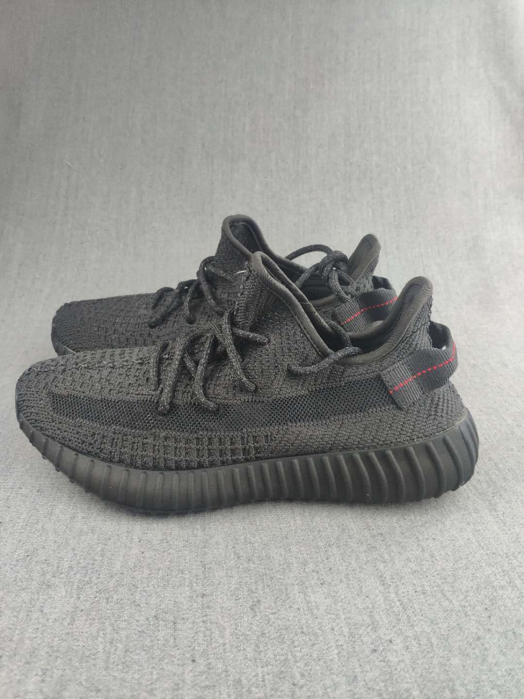 Black knit sneakers shown from a front-side angle with red heel stitching.