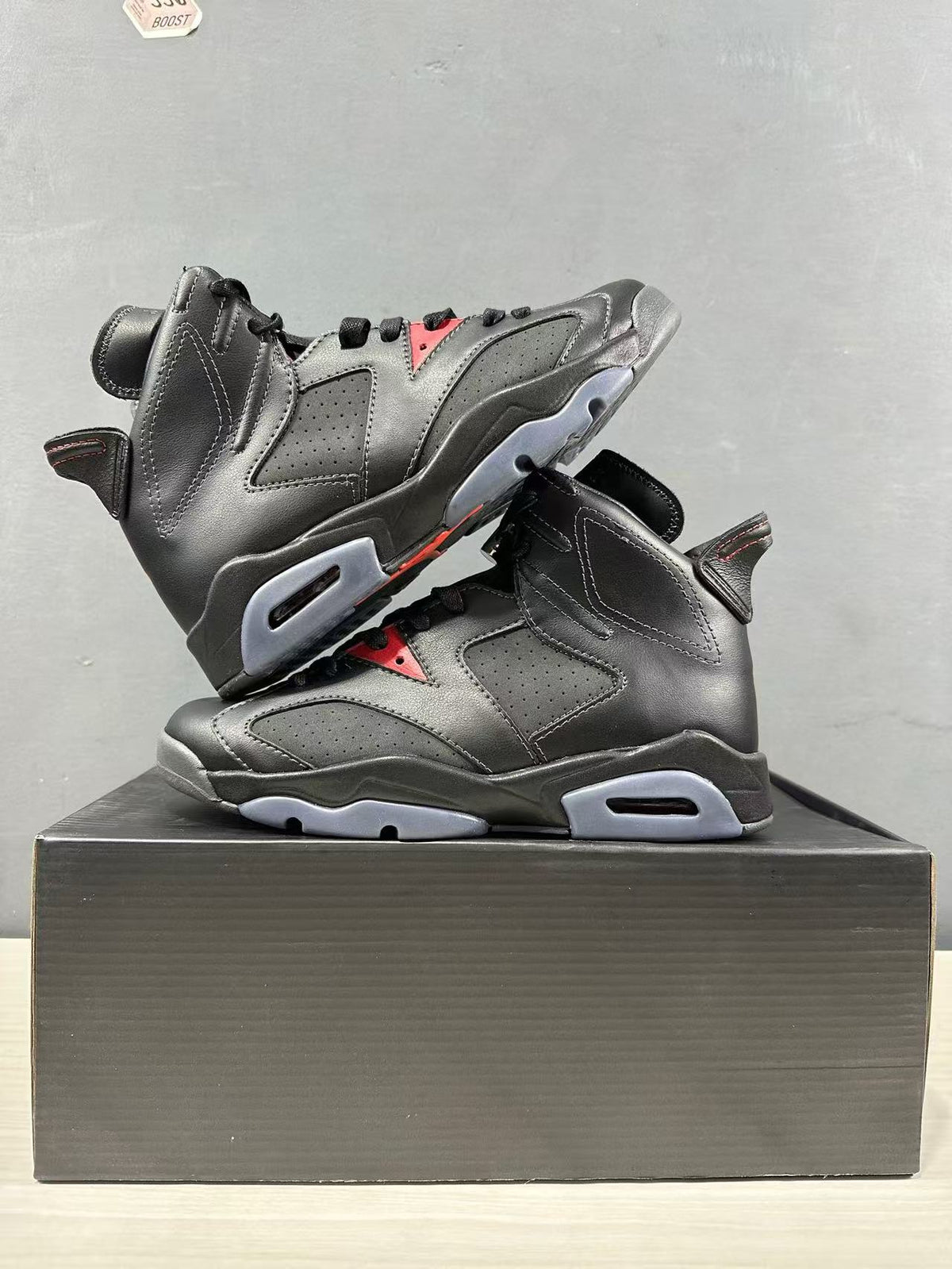 Angled view of two black sneakers highlighting the high collars, perforated panels, and red accents.