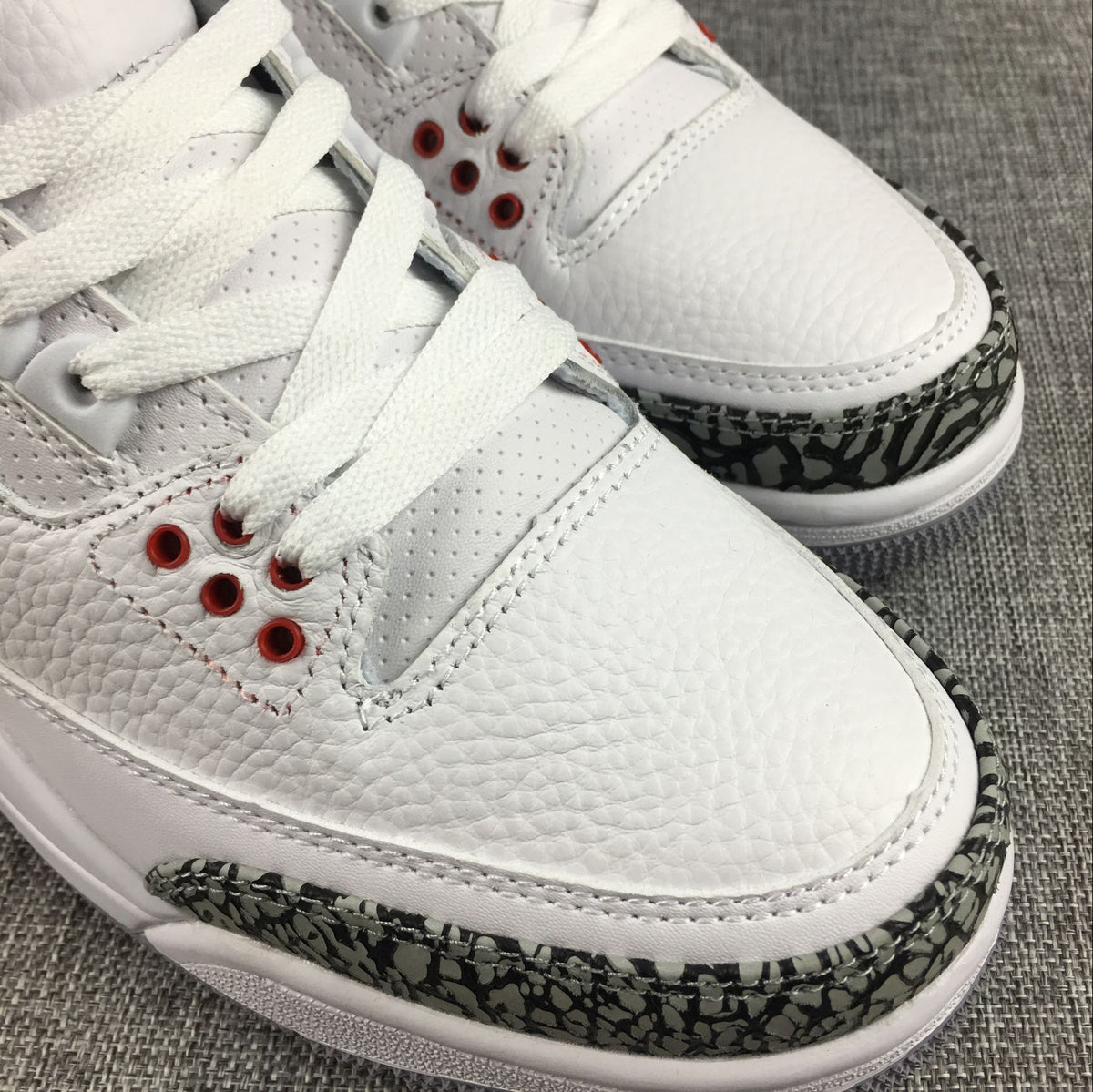 Close-up of the sneaker toe, white laces, red eyelets, and grey elephant-print overlay