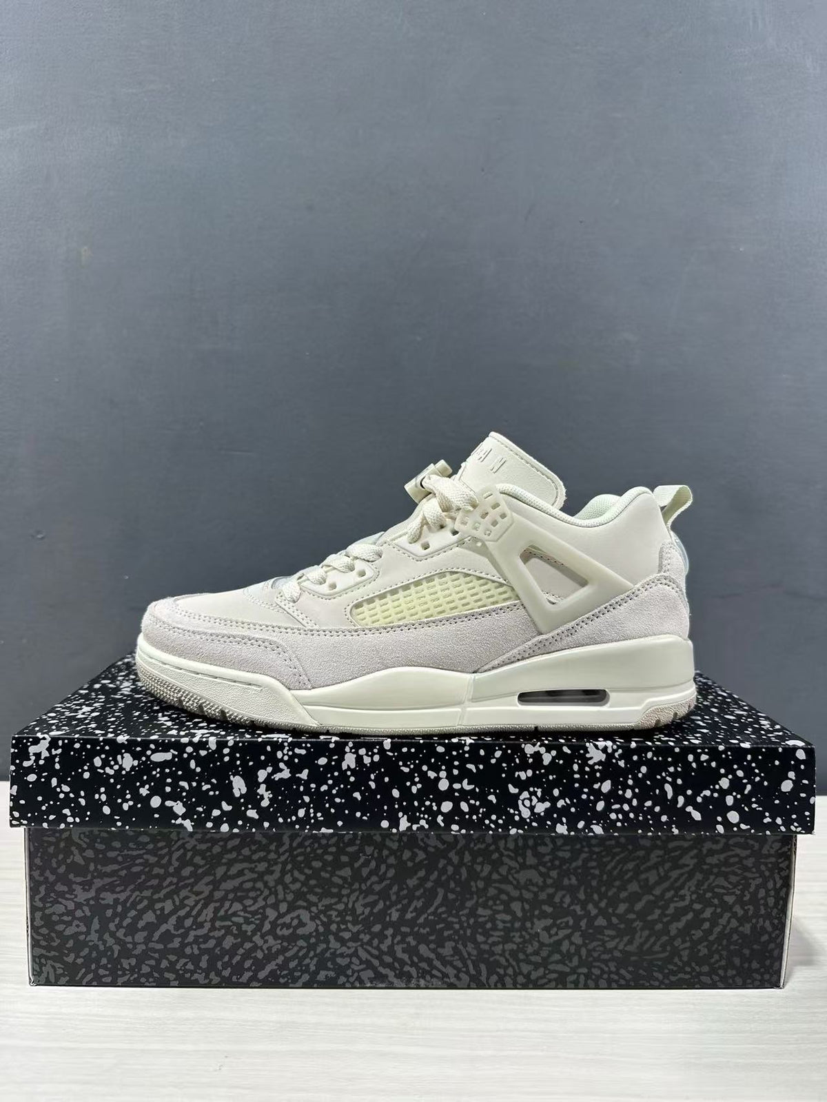 Side profile of one white and light grey sneaker on a patterned shoebox.