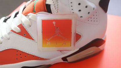 Side close-up showing the white and orange upper, perforated panel, accessory hangtag, and midsole cushioning detail.