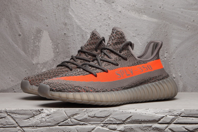 Side view of a grey Yeezy 350 V2 sneaker with dark laces, bright orange stripe, and translucent ribbed outsole.