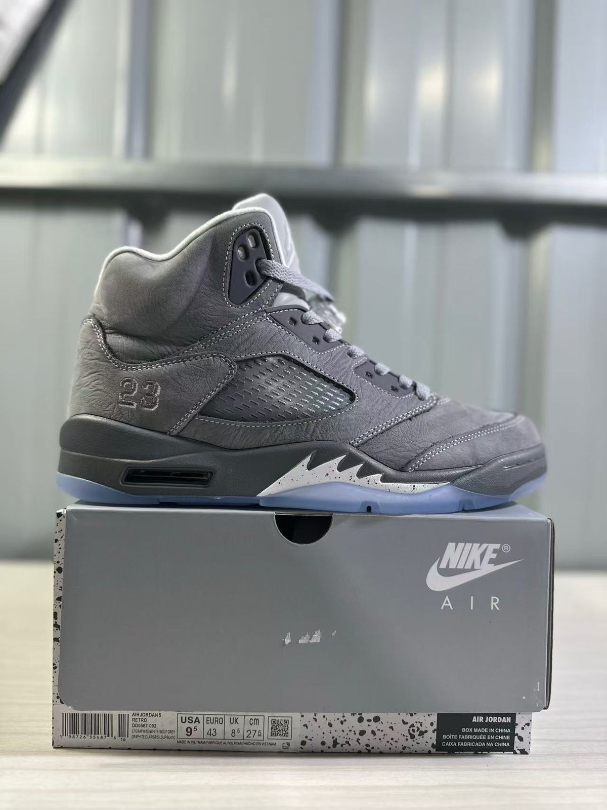 Side profile of a grey high-top sneaker displayed on its box; the box label visibly shows EU 43, US 9.5, UK 8, and CM 27.5.