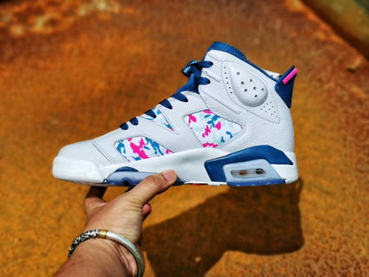 Side profile of a white sneaker with blue trim, multicolor patterned panels, and a visible heel air unit.