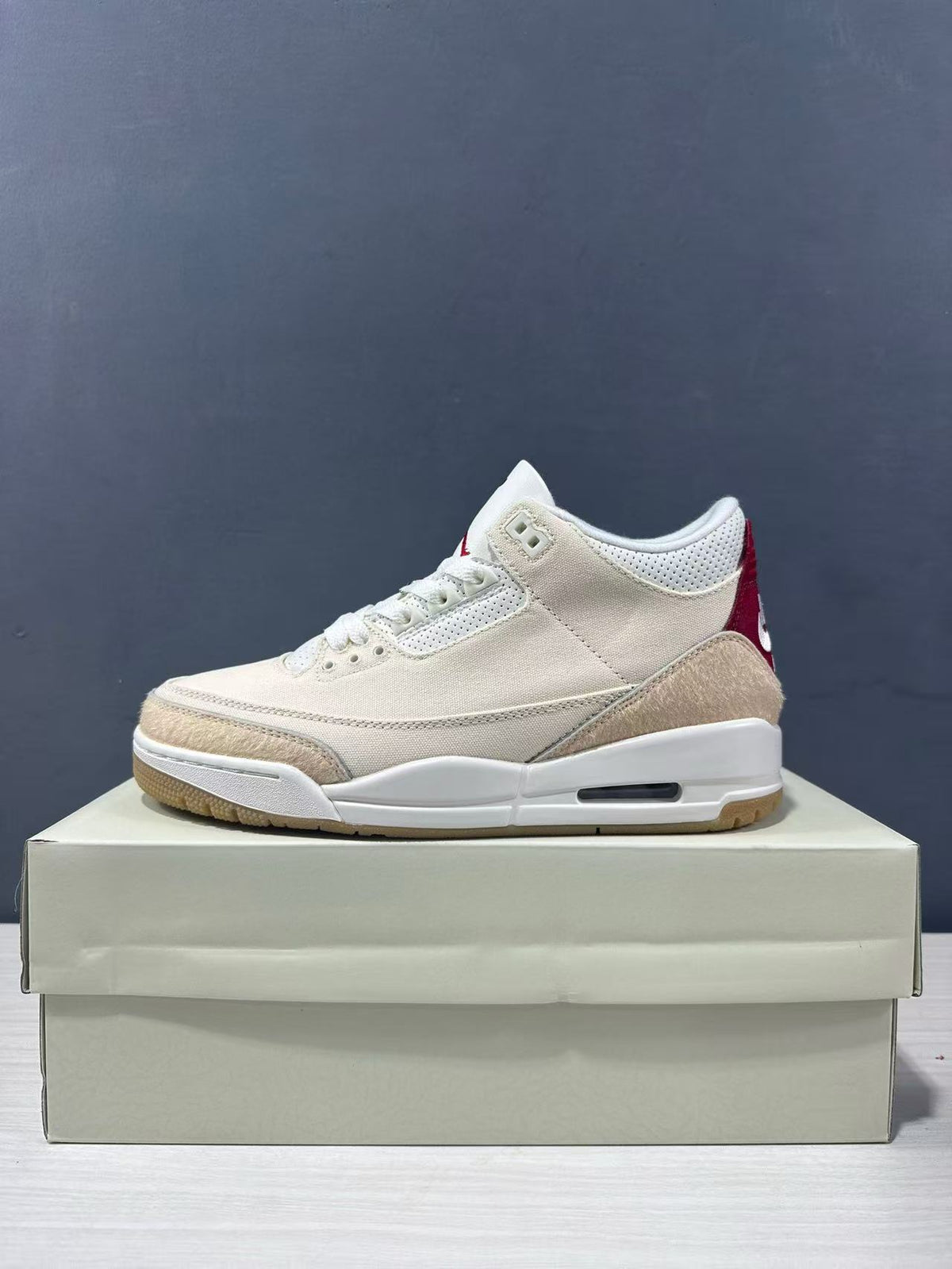 Clean lateral view of a cream Air Jordan 3 Retro sneaker with red heel detail, white midsole, and gum outsole.