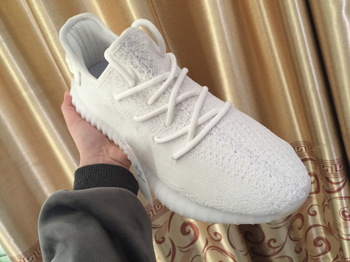 Handheld close-up of the white knitted upper, laces, padded collar, and rounded toe.