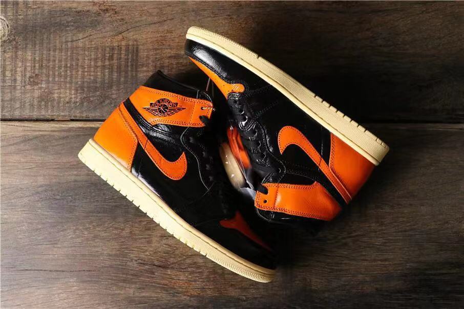 Two black and orange high-top sneakers arranged on a wood surface, showing their side profiles and cream-colored outsoles.