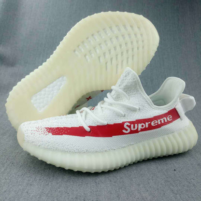 White low-top sneaker with a red side stripe, visible “Supreme” lettering, patterned upper, and translucent ribbed sole.
