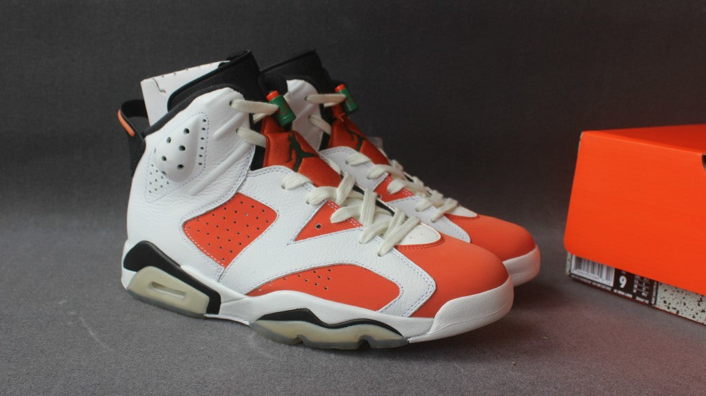 Three-quarter view of the pair beside the orange shoe box, showing the white and orange uppers and black accents.