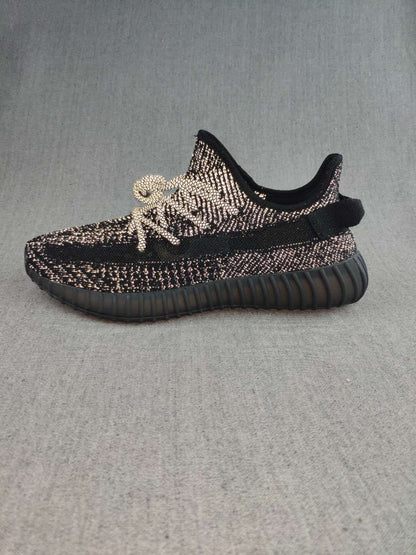 Side profile of a black Yeezy 350 V2-style sneaker with a dark ribbed sole.