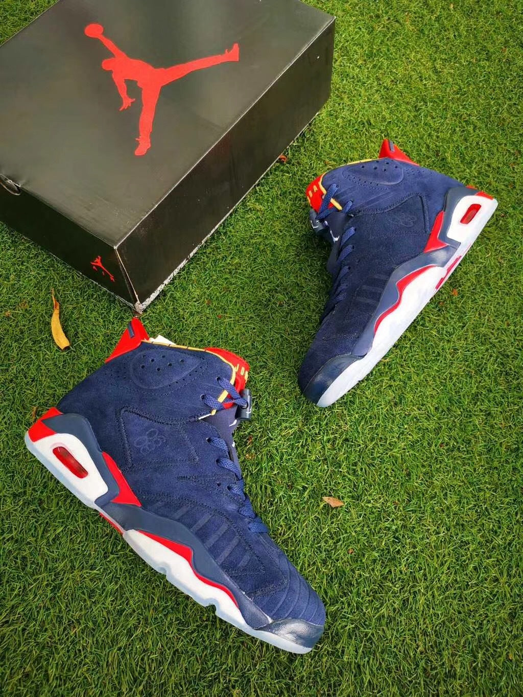 Two navy and red high-top sneakers displayed on grass beside a black Jordan shoebox.