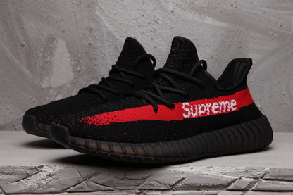 Pair of black knit-style low-top sneakers with red side stripes and white Supreme lettering.