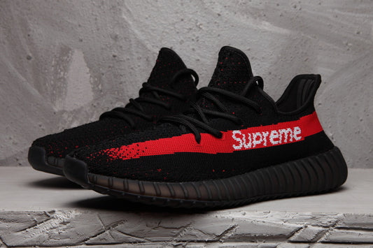 Pair of black knit-style low-top sneakers with red side stripes and white Supreme lettering.