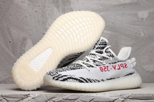 Side view of black-and-white patterned Yeezy 350 V2 sneakers, showing the ribbed off-white sole and red side text.