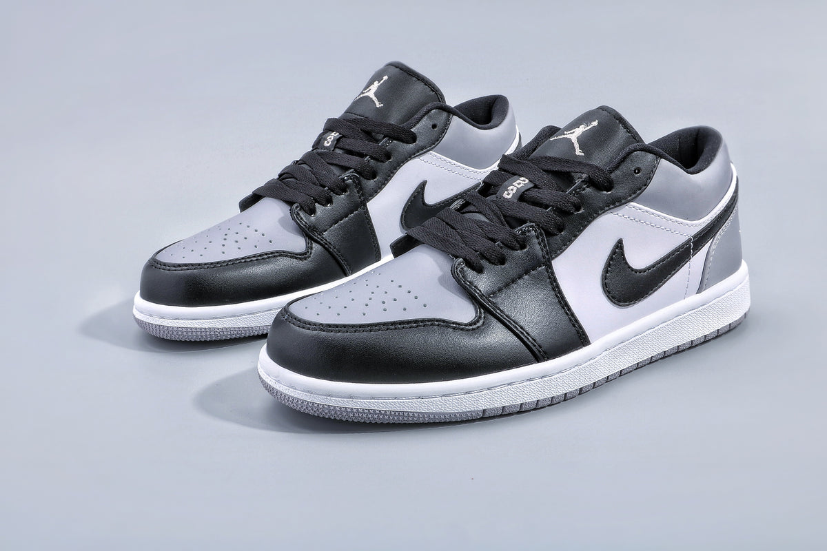 Pair of low-top black and grey Jordan 1 sneakers shown at an angle on a light grey background.