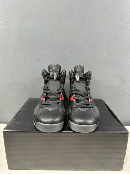 Front view of black Jordan mid-top sneakers with red accents, displayed on a black shoebox.