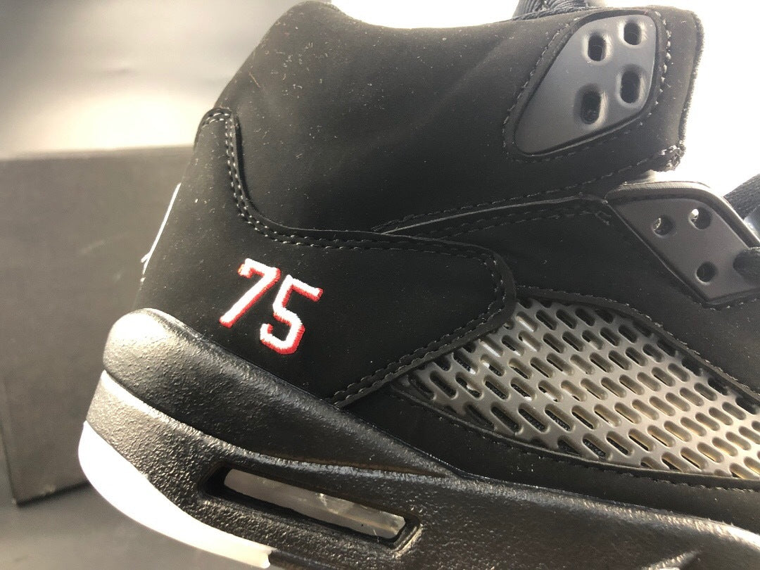 Close-up of the black upper, gray mesh panel, visible heel number 75, and midsole detail.