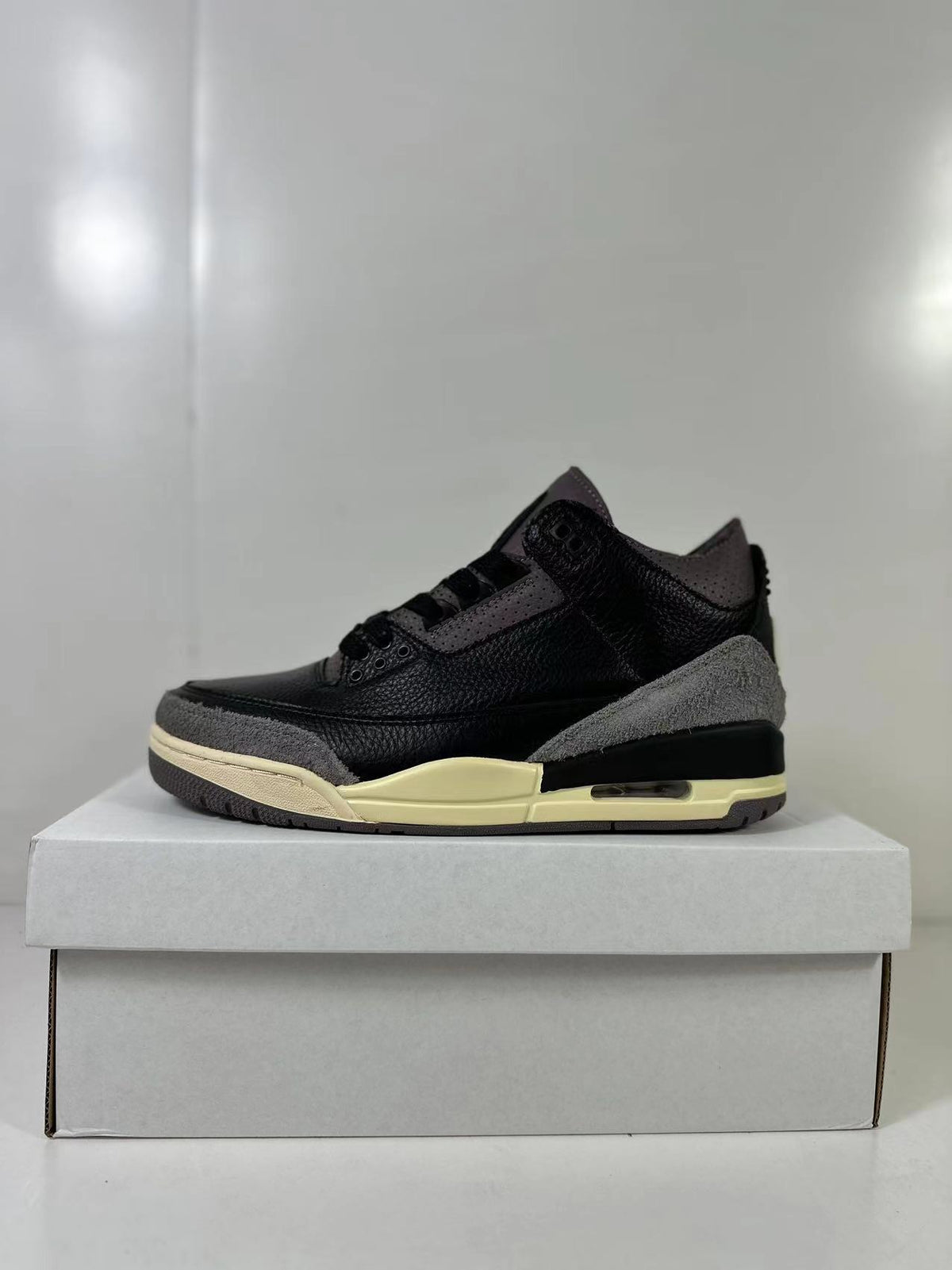 Side profile showing the black upper, gray heel and toe overlays, cream midsole, and heel cushioning window.