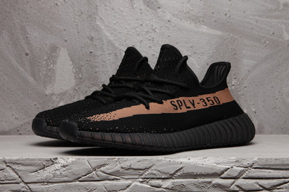 Pair of black Yeezy 350 V2-style sneakers viewed from the front side, showing the lace-up upper and contrasting side stripe.