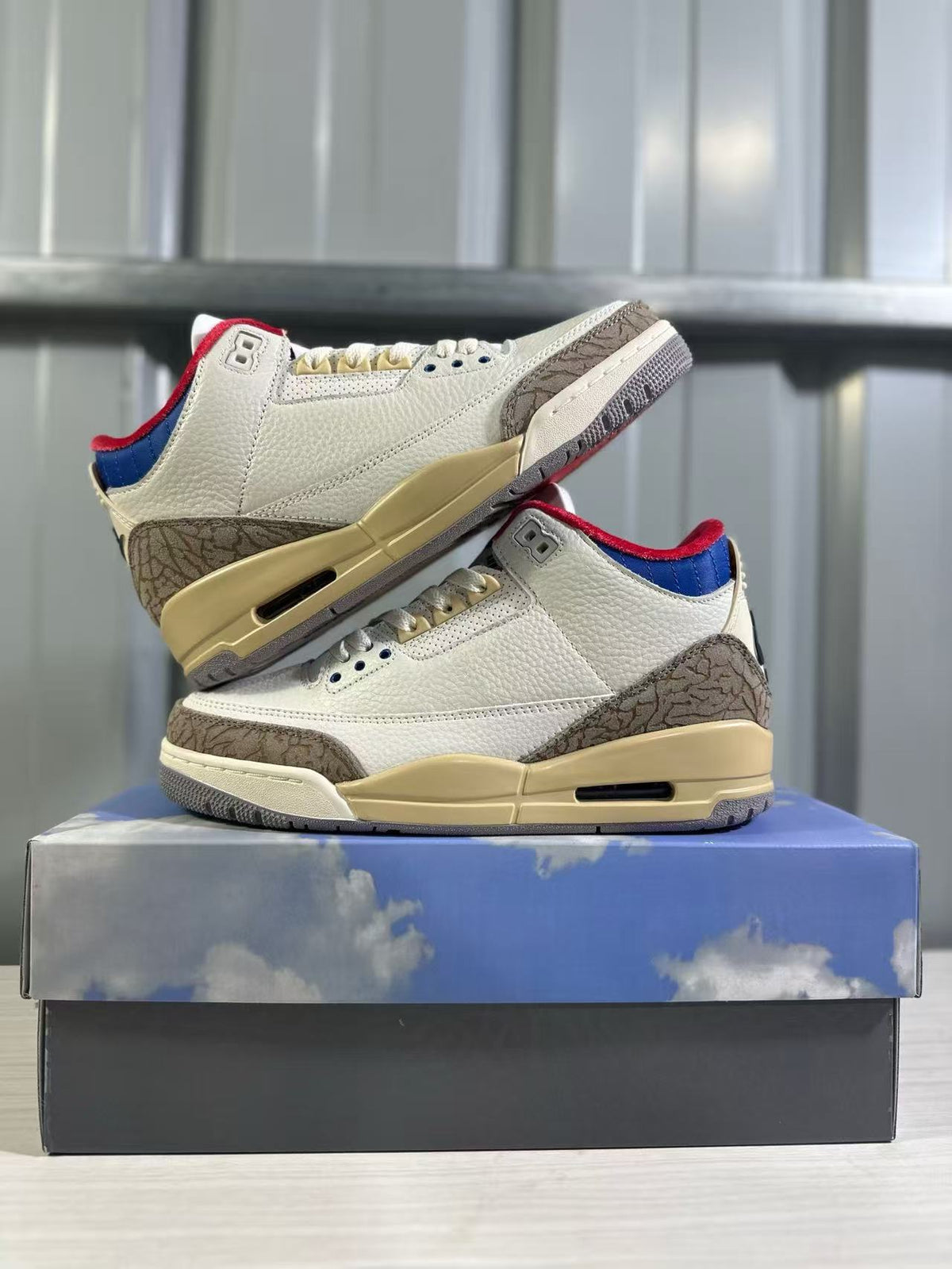 Side view of the white Jordan 3 sneakers displayed on a blue shoebox.