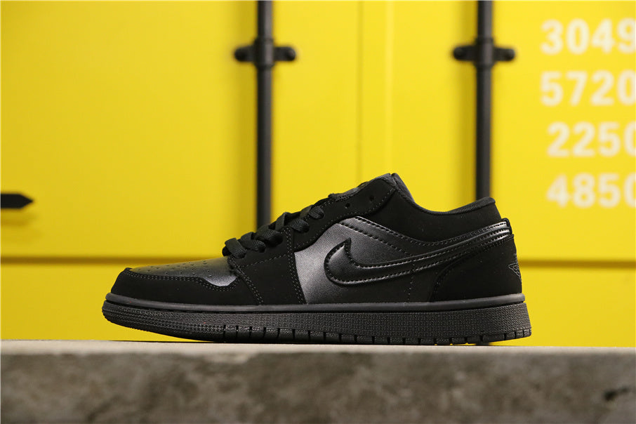Side view of an all-black low-top lace-up sneaker with a perforated toe box, textured side panels, and black rubber outsole.